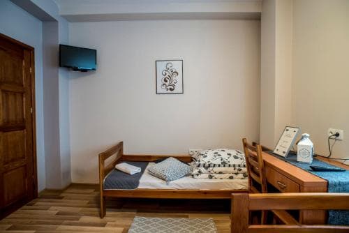 A cozy hotel room features a neatly made wooden bed, a desk with a chair, and a mounted TV, creating a comfortable and inviting atmosphere ideal for travelers seeking relaxation.