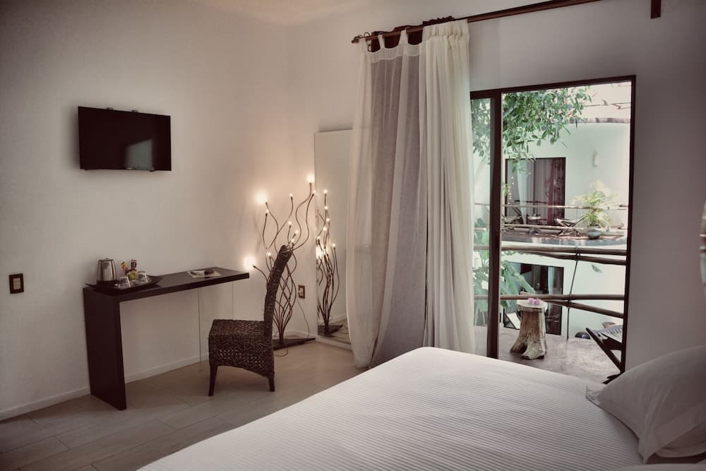 A serene hotel room features a cozy bed, modern desk setup, ambient lighting, and a balcony view of lush greenery, ideal for travelers seeking relaxation and comfort.