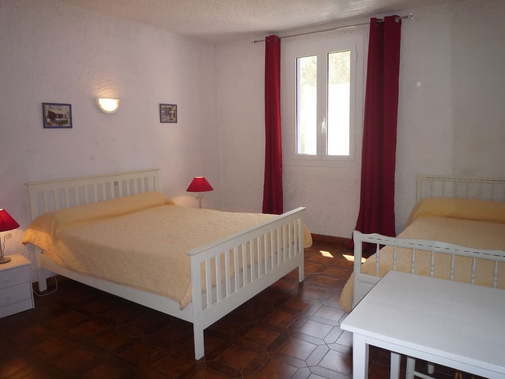 A cozy bedroom with white furniture, red curtains, and warm lighting offers a serene retreat for travelers seeking comfort in a vacation rental.
