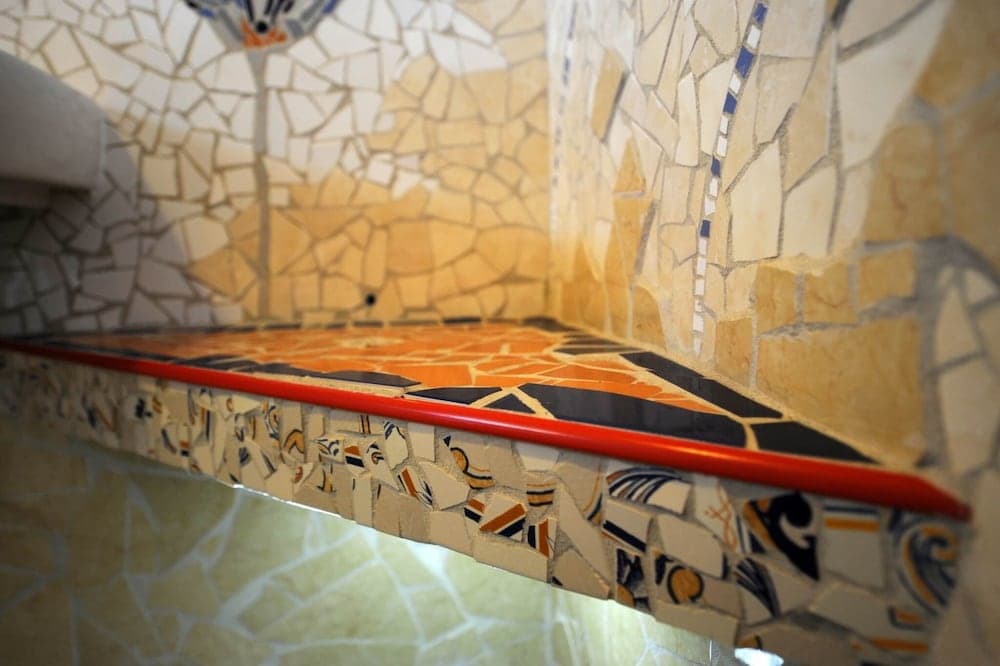 A vibrant mosaic-tiled bench with colorful patterns and a red railing sits within an artistic indoor space, ideal for travelers exploring unique architectural designs and cultural landmarks.