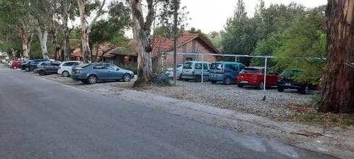 A serene roadside scene features parked cars along a tree-lined street near rustic houses, ideal for travelers seeking a quiet retreat in a natural setting.