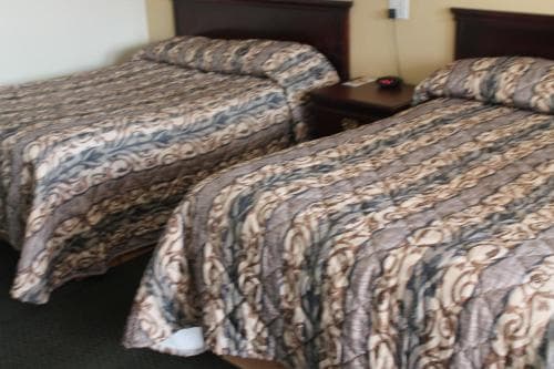 A cozy hotel room features two neatly made beds with patterned bedding, a small nightstand, and a warm ambiance, ideal for travelers seeking comfortable accommodations.