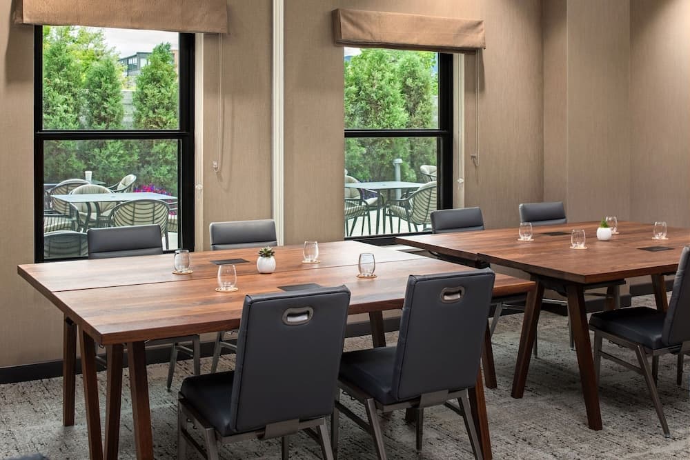 A cozy conference room with wooden tables, modern chairs, and large windows offering a serene view of greenery, ideal for business meetings or retreats.