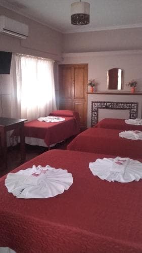 A cozy hotel room with neatly arranged beds covered in red linens, white towels folded decoratively, wooden furniture, and soft natural light filtering through sheer curtains, ideal for travelers seeking comfort and simplicity.