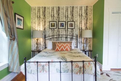 A cozy bedroom with green walls, birch tree-patterned wallpaper, and a floral bedspread exudes warmth and comfort, ideal for travelers seeking a serene retreat.