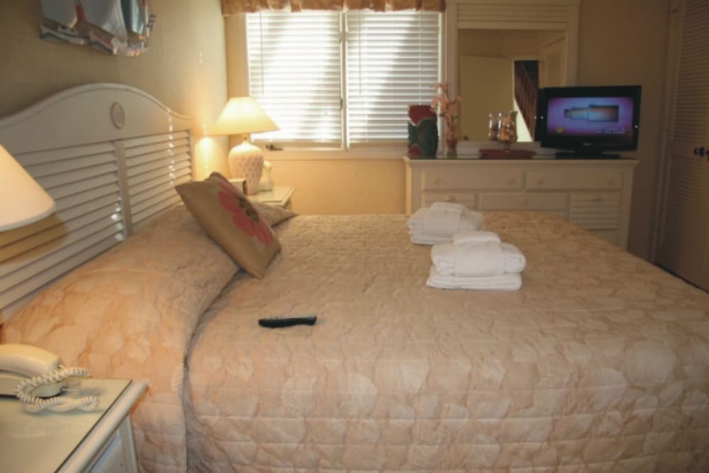 A cozy hotel bedroom with neatly arranged towels on the bed, soft lighting from bedside lamps, and a television on a dresser, ideal for travelers seeking comfort and relaxation.
