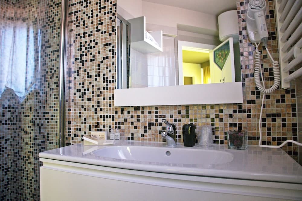 A cozy bathroom with mosaic-tiled walls, a sleek white vanity, and a mounted hairdryer offers a modern and inviting space for travelers seeking comfort and style.