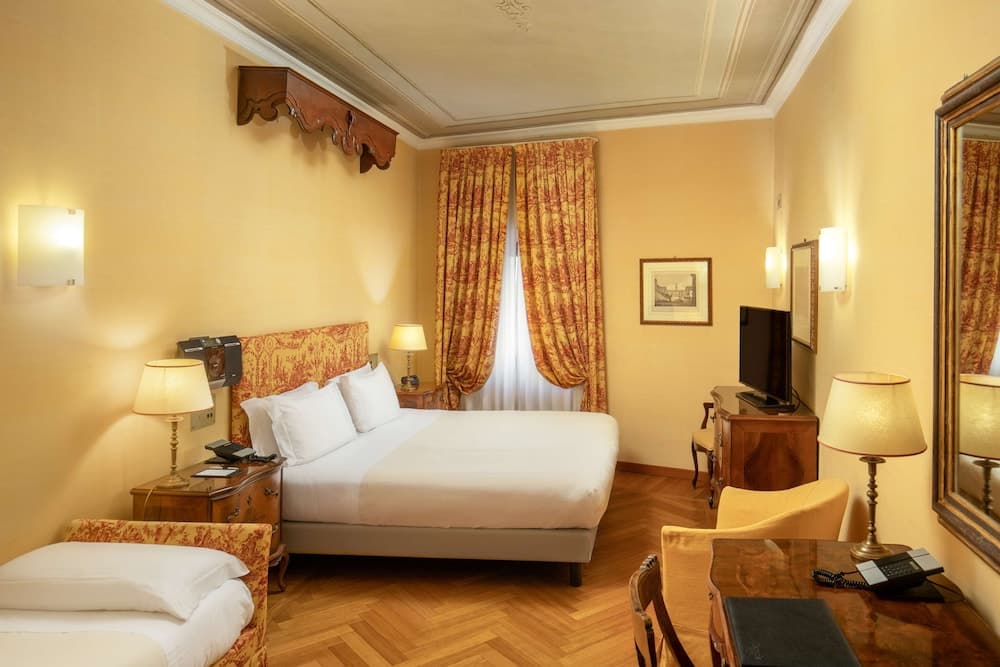 A cozy hotel room with warm yellow walls, elegant wooden furniture, plush bedding, and decorative curtains creates an inviting atmosphere ideal for travelers seeking comfort and relaxation.