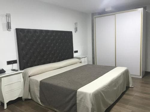 A cozy hotel room features a neatly made bed with a tufted headboard, white wardrobes, and soft lighting, creating a serene atmosphere ideal for travelers seeking comfort and relaxation.