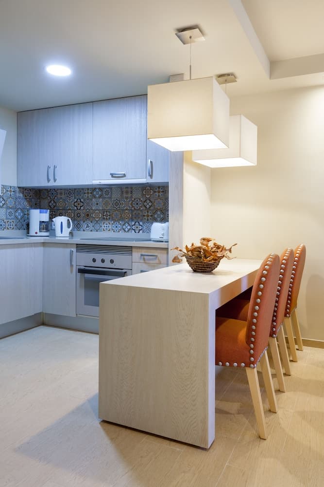 A modern kitchen with sleek cabinets, patterned backsplash, and a cozy dining nook illuminated by stylish pendant lights, ideal for travelers seeking a comfortable self-catering accommodation.