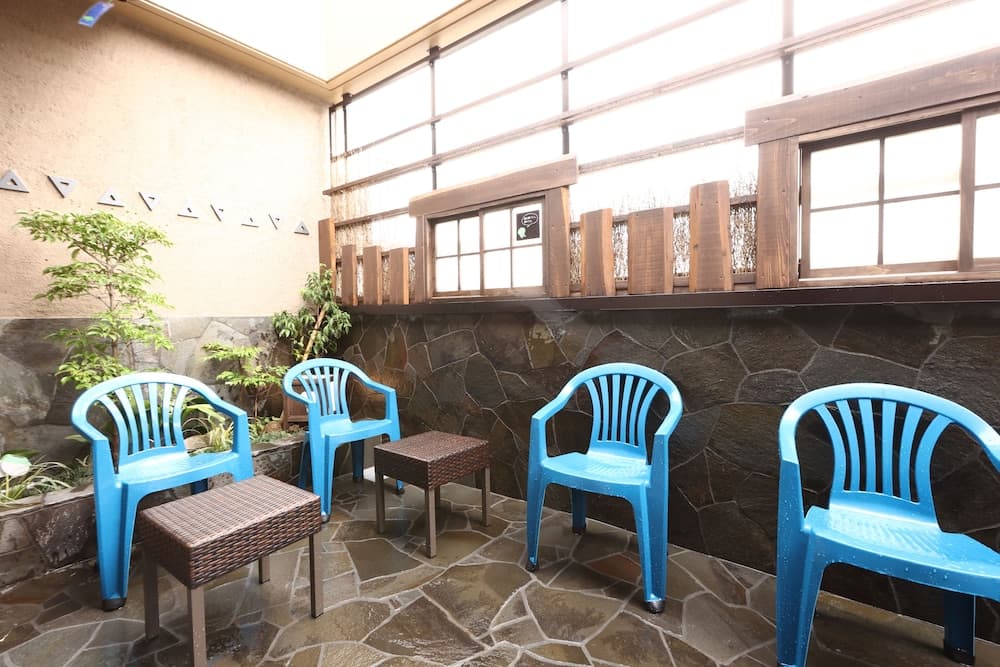 A serene indoor patio features blue plastic chairs around wicker tables, set against a stone wall with wooden accents and plants, ideal for travelers seeking a quiet relaxation spot.