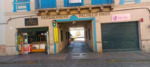 A vibrant street scene featuring a parking entrance labeled "Parqueadero Pacheco Hermanos" with colorful storefronts and closed shutters, ideal for urban exploration and local culture immersion.