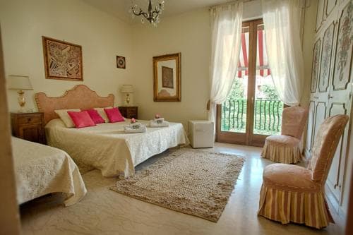 A cozy, well-lit hotel room features elegant furnishings, soft pink accents, and a balcony view, ideal for travelers seeking comfort and charm in a serene retreat.