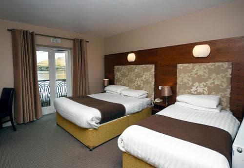 A cozy hotel room with two neatly arranged beds, patterned headboards, and a balcony overlooking water, ideal for travelers seeking comfort and scenic views.