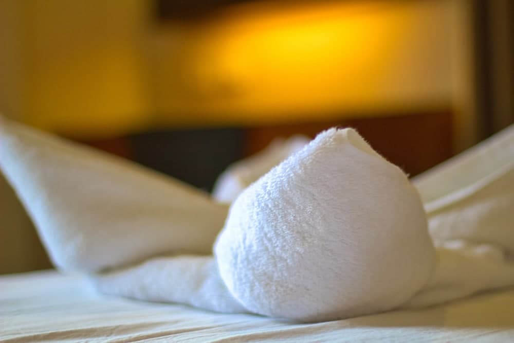 A cozy hotel room ambiance is captured with plush white towels artfully folded on a bed, set against warm, inviting lighting, ideal for travelers seeking relaxation and comfort.