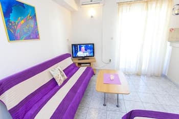 A cozy apartment interior features a vibrant purple sofa, a wooden coffee table, and a TV, creating a welcoming atmosphere ideal for travelers seeking comfort and relaxation.