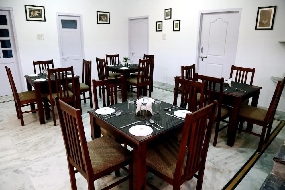 A cozy indoor dining area with wooden tables set for meals, framed animal artwork on white walls, and multiple doors, ideal for travelers seeking a quiet restaurant or hotel dining experience.