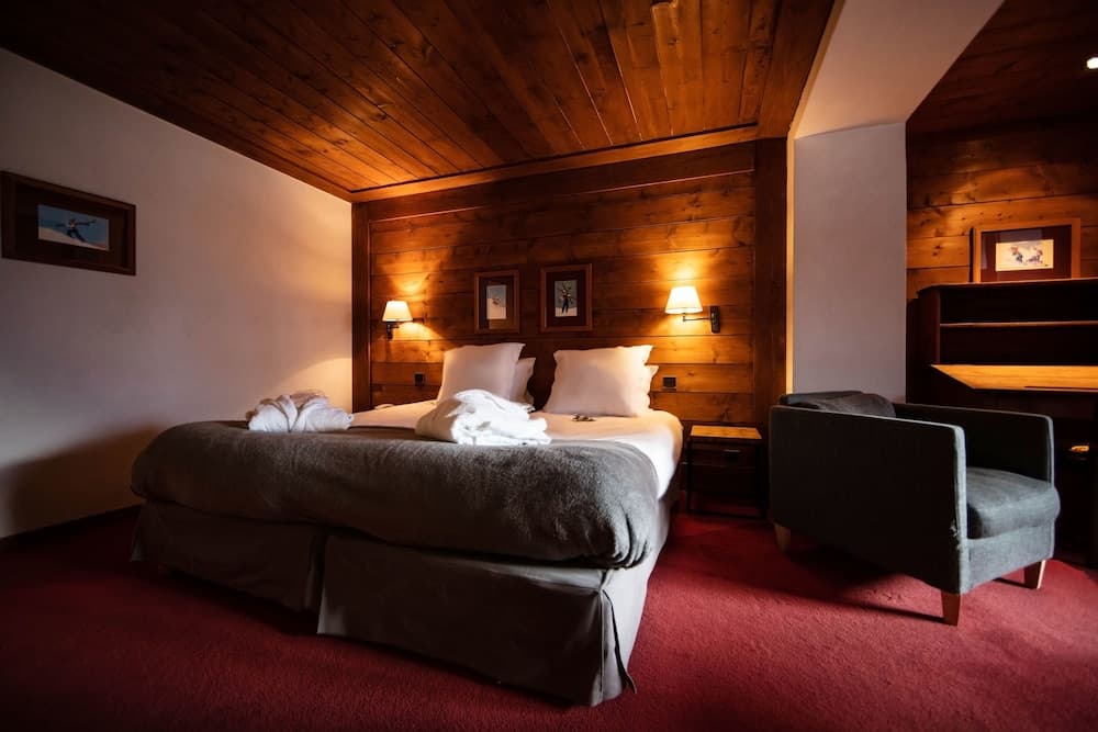 A cozy hotel room with wooden accents, warm lighting, and neatly arranged towels on the bed invites travelers seeking comfort and relaxation in a rustic setting.