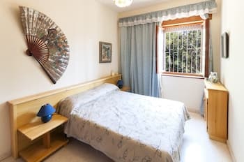 A cozy bedroom with soft lighting, wooden furnishings, and a decorative fan on the wall offers a serene retreat, ideal for travelers seeking relaxation in a quaint accommodation setting.