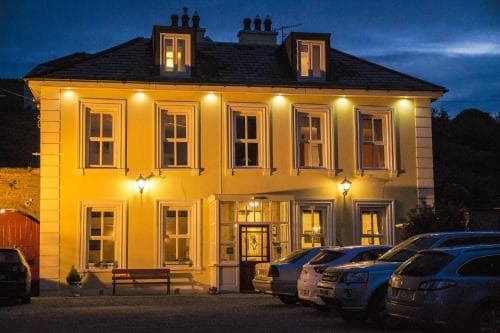 A warmly lit, two-story yellow building with multiple windows and a welcoming entrance glows invitingly at dusk, ideal for travelers seeking cozy accommodation in a quaint town setting.