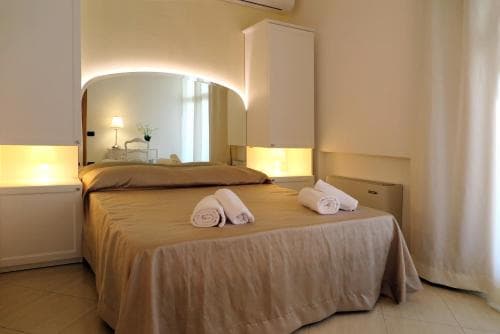 A cozy hotel room features a neatly made bed with rolled towels, soft lighting from bedside lamps, and a mirrored wall, creating a warm and inviting atmosphere ideal for travelers seeking comfort and relaxation.