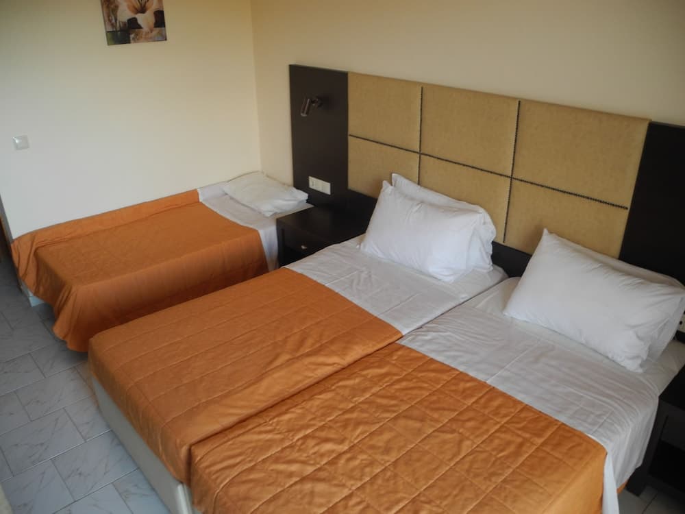 A cozy hotel room features two neatly made beds with orange quilts and white pillows against a modern headboard, ideal for travelers seeking comfort and simplicity.