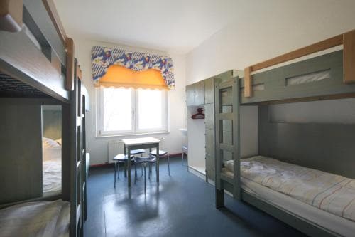 A cozy hostel room with bunk beds, a small table by the window, and vibrant curtains creates a welcoming atmosphere ideal for budget travelers seeking comfort and simplicity.