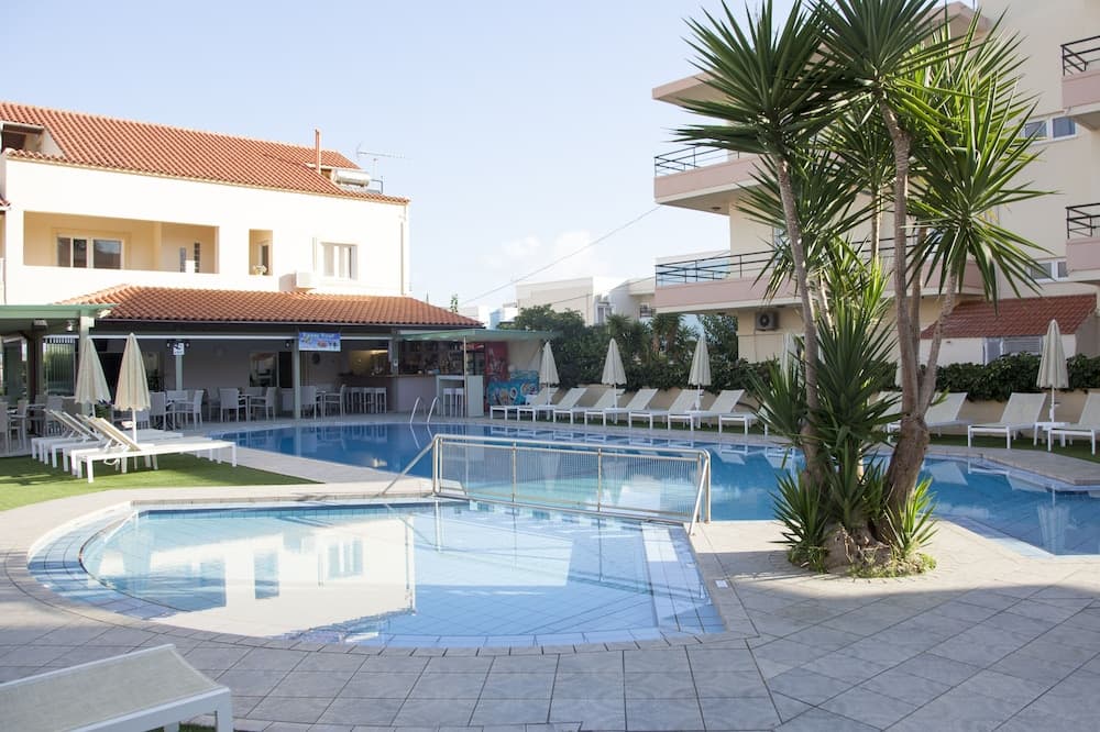 A serene resort pool area features clear blue water, white lounge chairs, palm trees, and a bar under a red-tiled roof, ideal for relaxing vacations in a tropical setting.