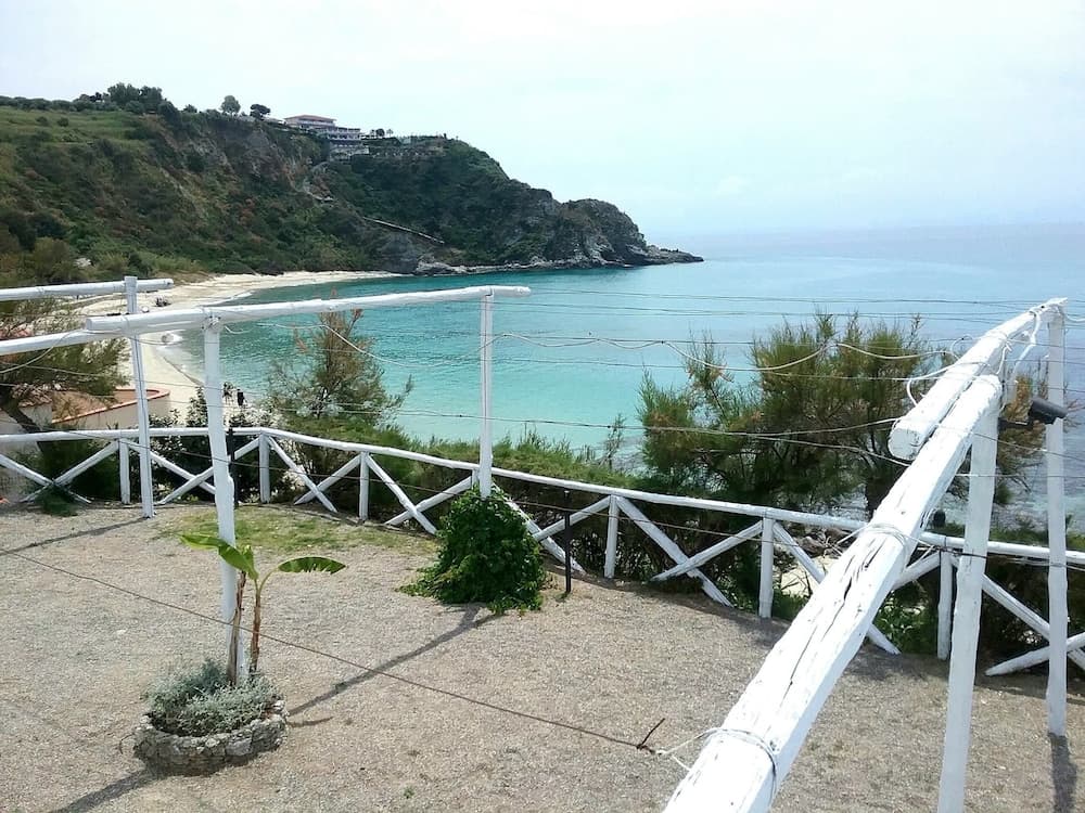 A serene coastal view framed by white wooden railings overlooks turquoise waters and lush green cliffs, ideal for tranquil beachside relaxation.