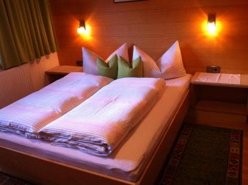 A cozy hotel room features a neatly made bed with green and white pillows, warm ambient lighting, and patterned carpeting, ideal for travelers seeking comfort and relaxation.