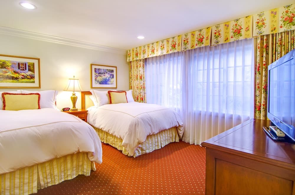 A cozy hotel room features two neatly made beds with floral curtains, warm lighting, and a flat-screen TV, ideal for travelers seeking comfort and relaxation.