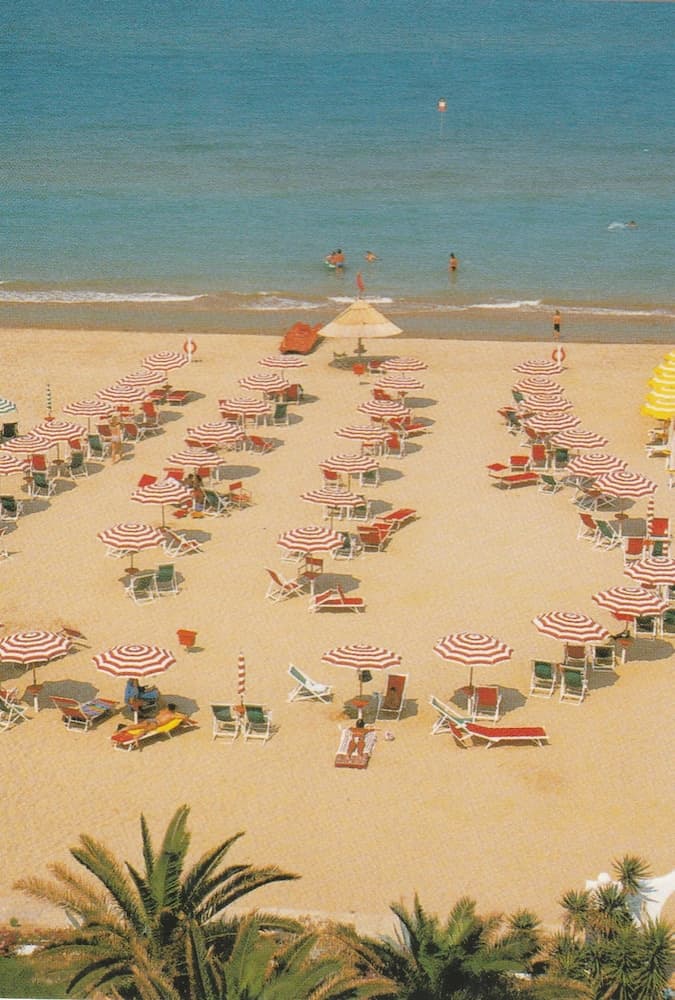 A serene beach scene with rows of red-and-white striped umbrellas and lounge chairs under the sun, ideal for a relaxing seaside getaway.