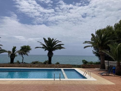 A serene coastal resort features a tranquil pool framed by palm trees under a partly cloudy sky, ideal for relaxing beachside vacations.