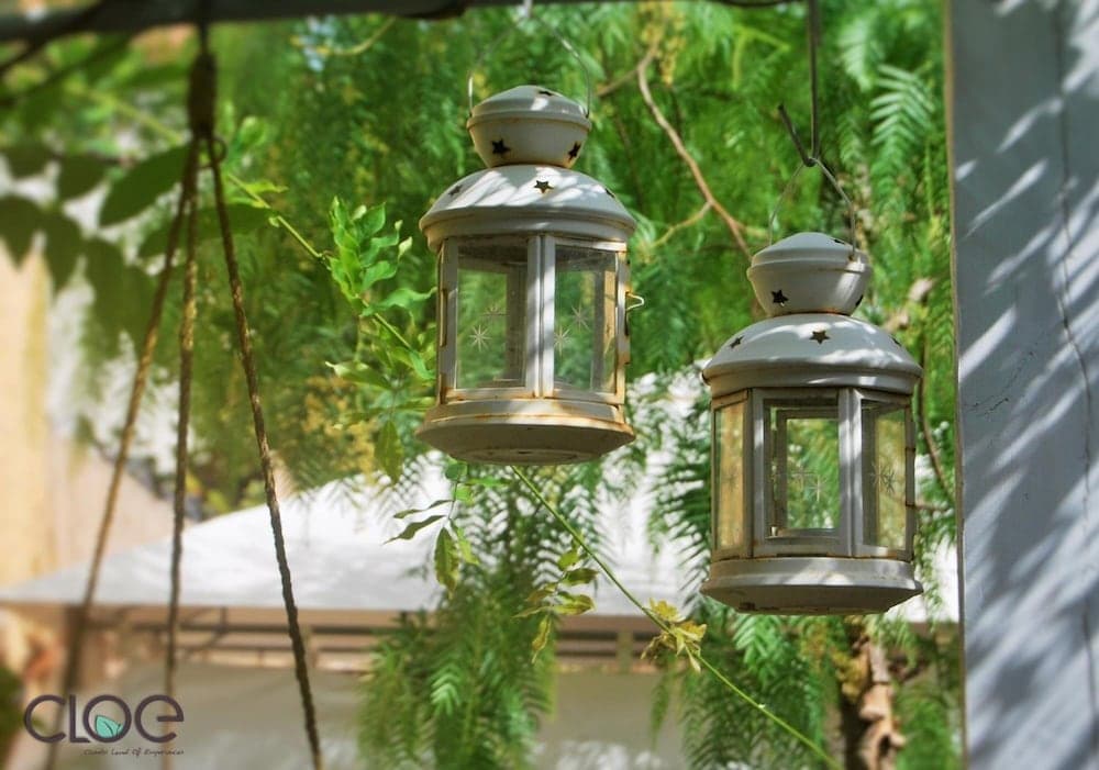 Two rustic white lanterns hang amidst lush greenery in a serene outdoor patio setting, ideal for travelers seeking a tranquil and picturesque spot for relaxation.