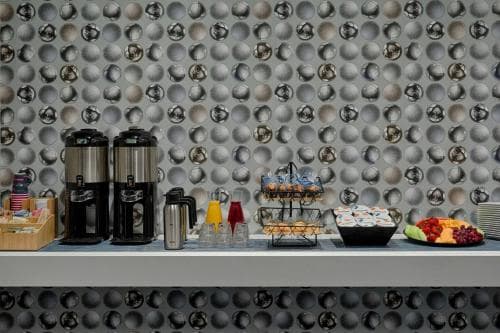 A modern hotel breakfast nook features a stylish wall of metallic spheres, a cozy counter lined with coffee makers, pastries, and fresh fruit, creating an inviting atmosphere for travelers seeking convenience and comfort.