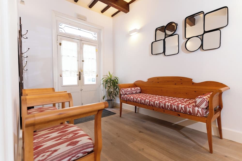 A cozy entryway features wooden furniture with patterned cushions, decorative mirrors on the wall, and a bright double door, ideal for travelers seeking a warm and inviting accommodation entrance.