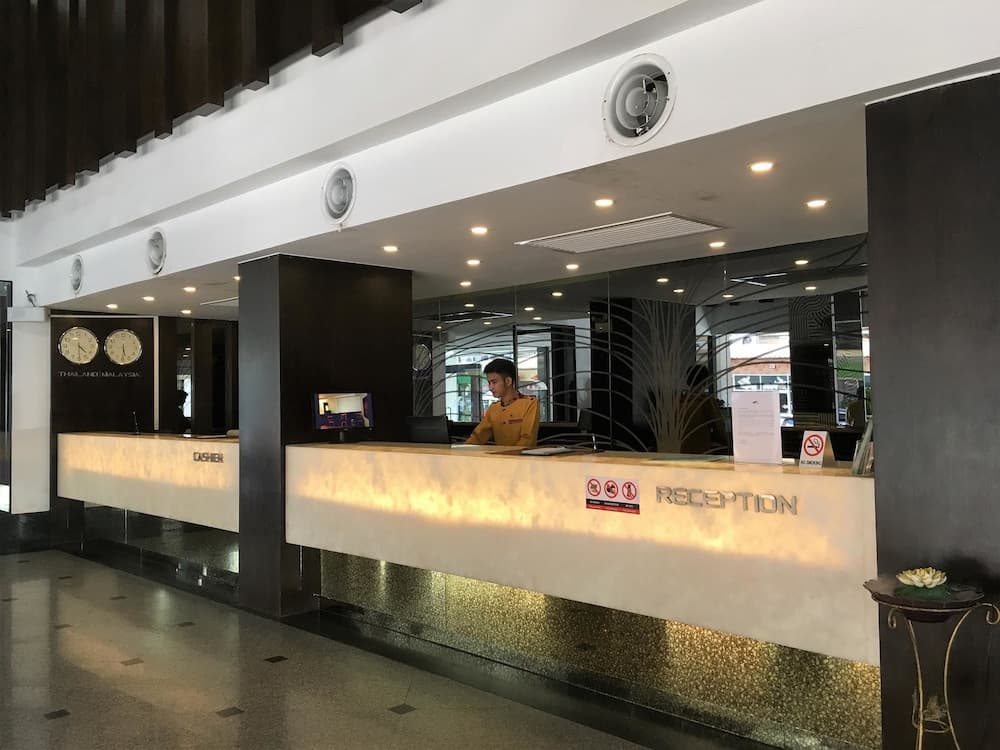 A modern hotel reception area features sleek white counters, a staff member in uniform, decorative clocks, and a tranquil water feature, ideal for travelers seeking a welcoming and professional check-in experience.