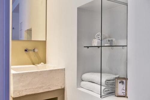 A modern bathroom features a sleek sink, mirrored cabinet with neatly folded towels, and a framed portrait, ideal for travelers seeking stylish accommodations.