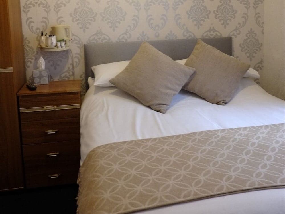 A cozy hotel bedroom features a neatly made bed with patterned bedding, a wooden bedside drawer, and decorative wallpaper, ideal for travelers seeking comfort and style.