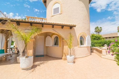 A charming Mediterranean villa courtyard features tiled floors, potted plants, and arched doorways under a sunny sky, ideal for a relaxing vacation retreat.