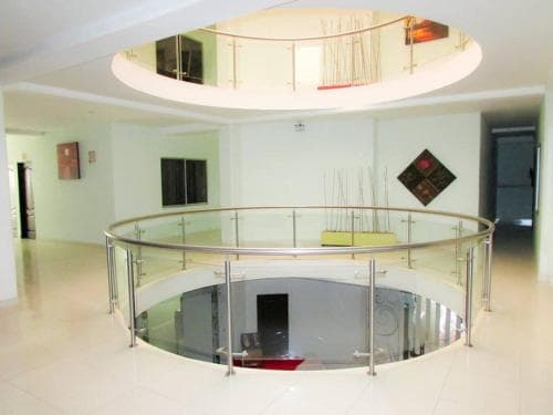 A modern indoor atrium features a circular glass railing overlooking a reflective lower level, creating an elegant and spacious atmosphere ideal for business or residential tours.