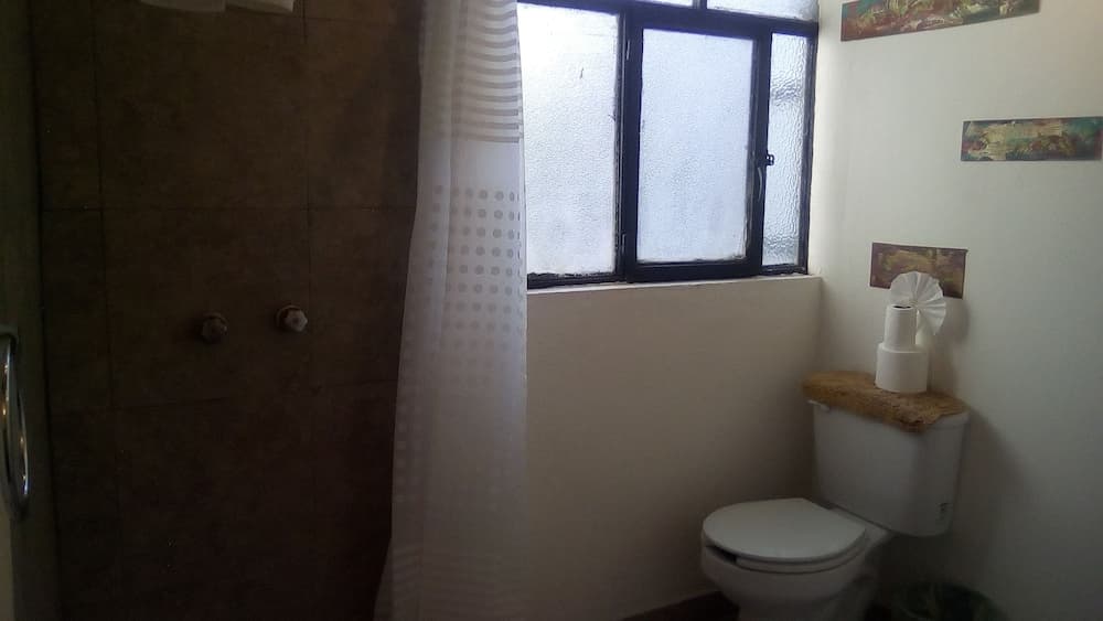 A cozy bathroom with a frosted glass window, tiled shower, white toilet topped with neatly stacked toilet paper, and simple decor creates a functional and serene space ideal for travelers seeking comfort.