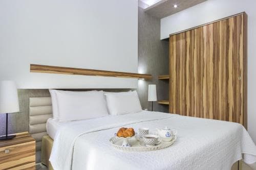 A cozy hotel room features a neatly made bed adorned with a breakfast tray, set against modern decor with wooden accents, ideal for travelers seeking comfort and convenience.