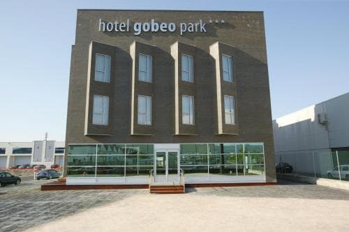 The modern facade of Hotel Gobeo Park stands prominently under a clear sky, featuring sleek glass windows and a welcoming entrance, ideal for travelers seeking a stylish urban stay.