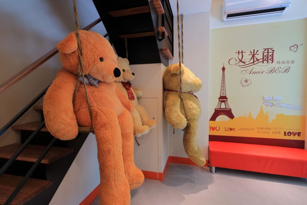 A cozy B&B entrance features oversized teddy bears hanging near a staircase, alongside a vibrant red bench and Paris-themed wall art, creating a charming and welcoming atmosphere ideal for romantic getaways.