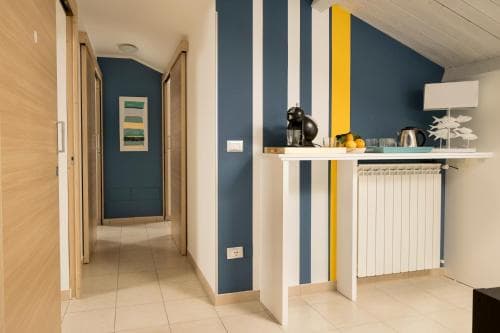 A cozy apartment interior features vibrant blue and yellow striped walls, a small white kitchen bar with fruit and decor, and a hallway leading to a bedroom, ideal for travelers seeking a stylish and comfortable stay.