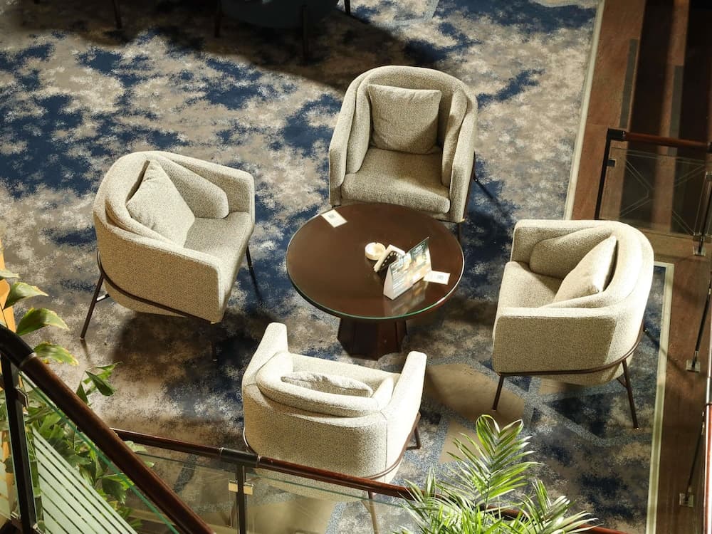 A cozy lounge area with modern armchairs arranged around a glass-top table on a patterned carpet, ideal for travelers seeking a relaxing spot in a hotel or airport lounge.