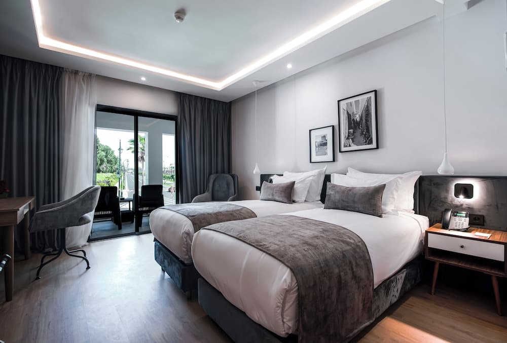 A modern hotel room with twin beds, sleek furniture, and a balcony view of greenery offers a cozy and stylish retreat for travelers seeking comfort and relaxation.
