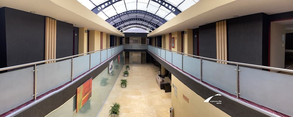 A serene hotel atrium features a spacious two-story layout with glass railings, potted plants, and a skylight, ideal for travelers seeking a calm and modern accommodation experience.