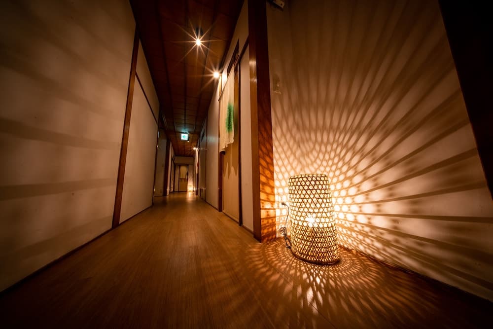 A serene hotel corridor bathed in warm light from a woven lamp casts intricate shadows on the walls, creating an inviting and tranquil atmosphere ideal for relaxation and mindfulness retreats.